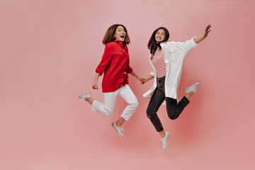 Happy women jump on isolated background. Tanned Asian girls in stylish outfits move on pink backdrop.