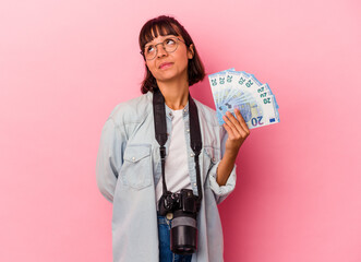 Young mixed race photographer woman holding bills isolated on pink background dreaming of achieving...