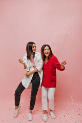 Happy charming girls in oversized white and red shirts laugh and pose on pink background with bubbles and confetti.