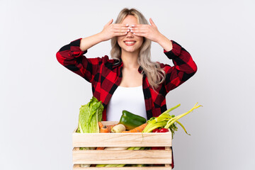 Farmer girl holding a basket full of fresh vegetables over isolated white background covering eyes...