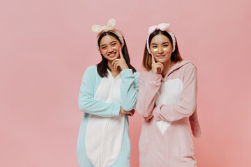 Happy brunette Asian girls in kigurumis smile sincerely on isolated. Young women in pajamas and...