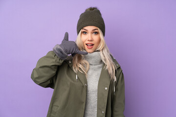 Teenager blonde girl with winter hat over isolated purple background making phone gesture. Call me back sign