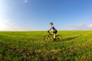 Fototapeta na wymiar The cyclist rides a bicycle on the green grass on the field. Outdoor sports. Healthy lifestyle.