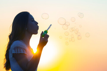 woman blows bubbles against the backdrop of the setting sun. summer fun and outdoor recreation