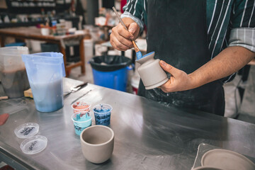 young adult potter painting pieces of clay
