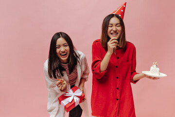 Joyful brunette Asian women laugh on pink isolated background. Lady in party hat and red blouse...