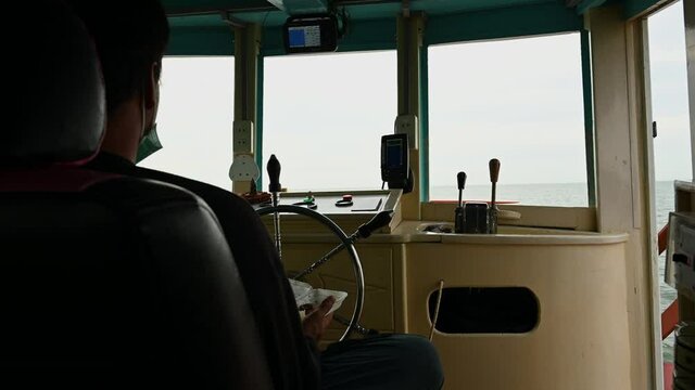 a silhouette of Pilot seen from its back eating something while maneuvering the boat out to the ocean during a Whale Watching trip in the gulf of Thailand.