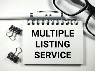 Text MULTIPLE LISTING SERVICE writing on notebook with pen,paper clips and glasses on white...