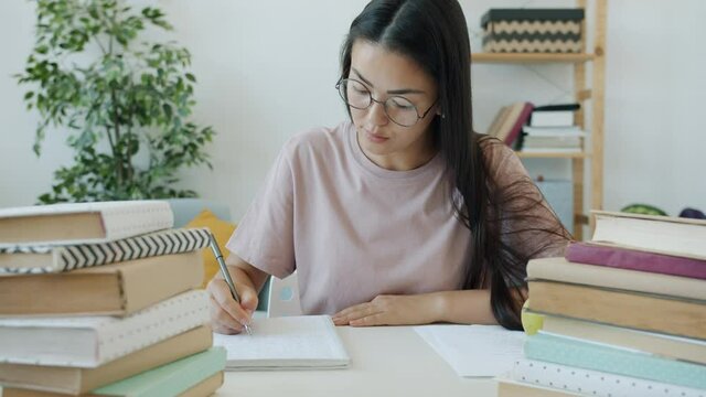 Slow motion of diligent student writing essay sitting at desk with books at home concentrated on education. Knowledge and smart youth concept.