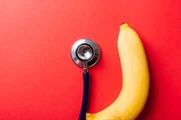 World sexual health or Aids day, Top view flat lay of doctor stethoscope and yellow banana, studio shot isolated on a pink background, Safe sex and reproductive health concept