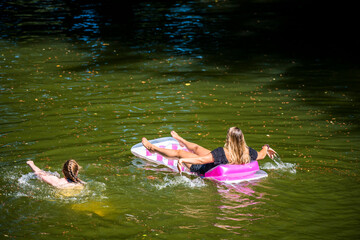 Mom and daughter are breathing on the water while swimming on a picturesque lake in the forest