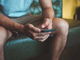 Hand man using smartphone. A young person, man in casual grey shirt and shorts sitting and interacting with technology at home. Relaxation businessman working online at anywhere concept.