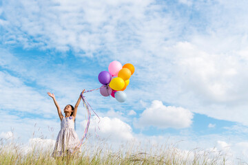 Cheerful cute girl holding balloons running on green meadow white cloud and blue sky with happiness. Hands holding vibrant air balloons play on birthday party happy times summer on sunlight outdoor - obrazy, fototapety, plakaty