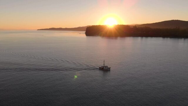 A aerial drone shot of a lone fishing trawler with sunset and coastline in the distance near Sooke, BC. 4K 24FPS.