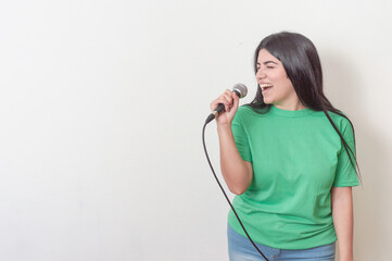 young white latin girl with black hair dressed in green with a microphone singing over a white background