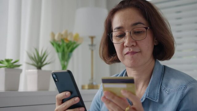 Asia hispanic senior people sit relax comfort smile at home sofa couch enjoy gift card typing wifi smart phone remotely buy on social media e-commerce retail shop store secure tech data omnichannel.