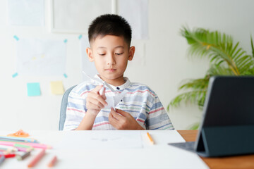 Asian boy playing paper airplane while sitting at home 