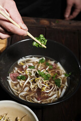 Chef adding greens with chopsticks to pho bo
