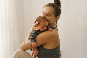 Mother holds and hugs her newborn baby son at home. Happy infant and mom.