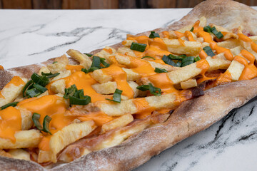 Delicious pizza. Closeup view of a cheddar and mozzarella cheese, french fries, green onion, tomato sauce and bacon pizza, on the white marble table. 