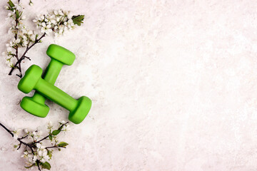 Green dumbbell with apple blossom branches on a light marble background.