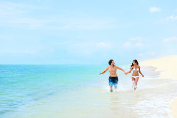 Beach vacation happy couple running splashing water in blue ocean having fun in Caribbean destination summer travel. Tourists enjoying holidays relaxing laughing together holding hands.