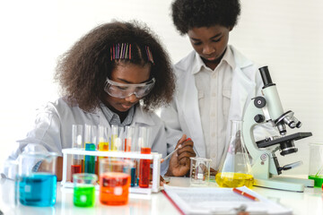 Two african american cute little boy and girl student child learning research and doing a chemical experiment while making analyzing and mixing liquid in test tube at science class in school