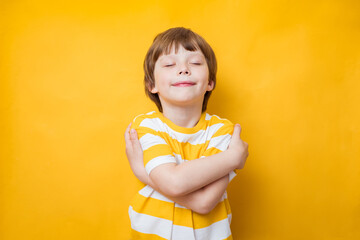 Cute kid boy smiling with pleasure while embracing himself, keeping arms around his shoulders. Body positive, self acceptance, self esteem concept