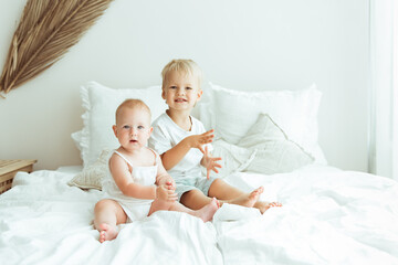 Little infant baby girl sitting together with her toddler brother on the bed