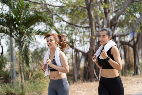 Young Asian women running outdoor and sweat wipes on neck in the park. Sport girl in sportswear running or jogging in summer day. Woman, Sport and exercise concept