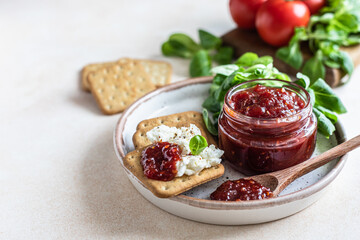 Tomato jam, confiture or sauce in glass jar with crackers and green leaves salad. Unusual savory jam. Mediterranean cuisine.