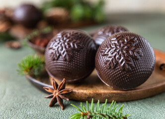 Tasty cocoa bombs with marshmallow and chocolate on wooden plate with fir branches and spices. Trendy winter hot drink.