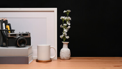 Photographer workplace with camera, picture frame, books and coffee cup on wooden table.