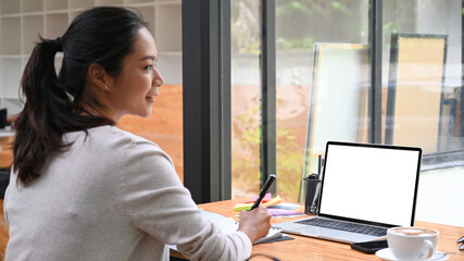 Back view happy woman working with laptop in modern workplace.