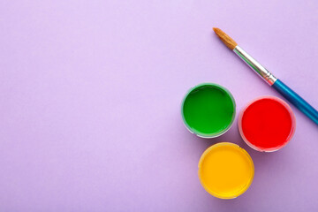 Multicolored jars of gouache and a brush on a purple background. Creative kit.