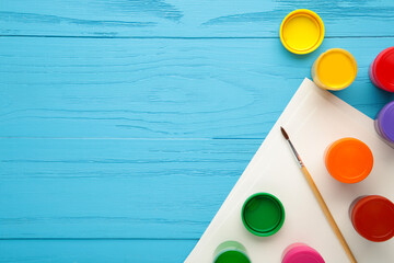 Multicolored jars of gouache and a brush on a blue background. Creative kit.