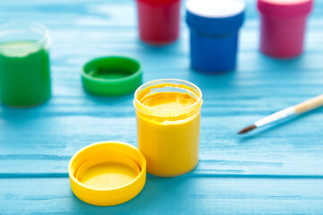 Multicolored jars of gouache and a brush on a blue background. Creative kit.
