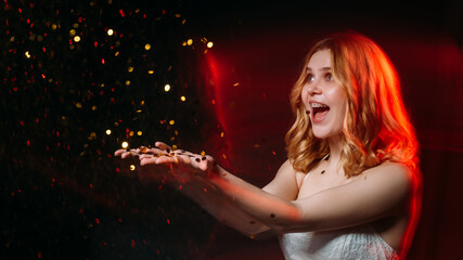 Make wish. Happy woman. Festive celebration. Holiday spirit. Excited beautiful laughing lady throwing golden confetti spangles isolated black long exposure red blur light copy space.