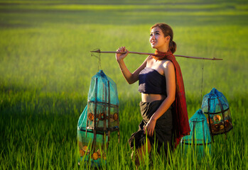 A rural young farmer in traditional dress and shawl works in the green rice fields.