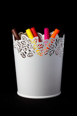 Colored markers in a white glass on a black background