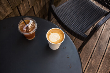 Cold iced coffee to go in clear plastic cup and fresh cappuccino with beautiful latte art. Take away summer drink concept. Tea and ice coffee glass on terrace table in cafe, cafeteria or coffee shop