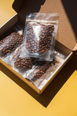 Roasted arabica sample coffee box with beans in blank transparent plastic bag with zipper on yellow background. Specialty and alternative trendy photo with shadow concept. Mock up, top view