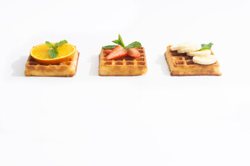 Belgium waffles with strawberry, banana and orange with syrup on white