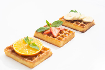 Belgium waffles with strawberry, banana and orange with syrup on white