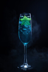 Cold blue cocktail with a star fruit garish on black background.