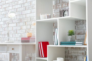 Shelf unit with books, candles and plant near brick wall
