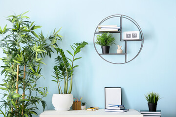 Table with books, frame and houseplants near color wall