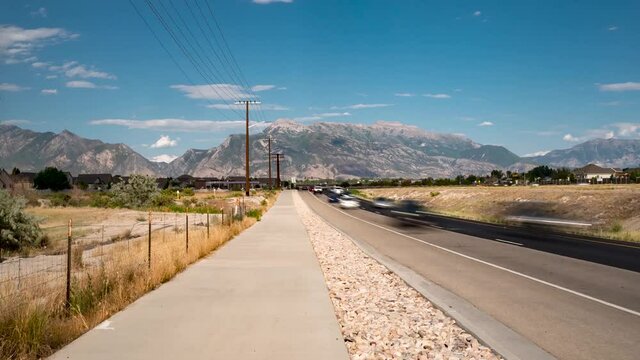 Cars and trucks driving along a busy street at rush hour with mountains in the background - zoom out time lapse