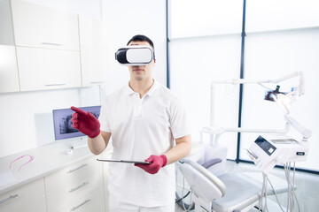A male dentist in uniform stands in the office and checks the digital image before the patient's...