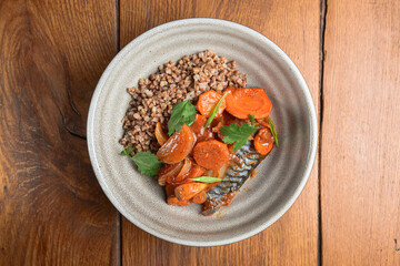 Buckwheat porridge with fish in a ceramic plate over rustic wooden background.
